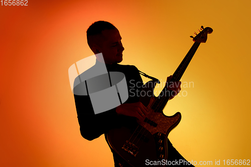 Image of Silhouette of young caucasian male guitarist isolated on orange gradient studio background in neon light