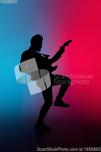 Image of Silhouette of young caucasian male guitarist isolated on blue-pink gradient studio background in neon light