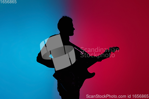 Image of Silhouette of young caucasian male guitarist isolated on blue-pink gradient studio background in neon light