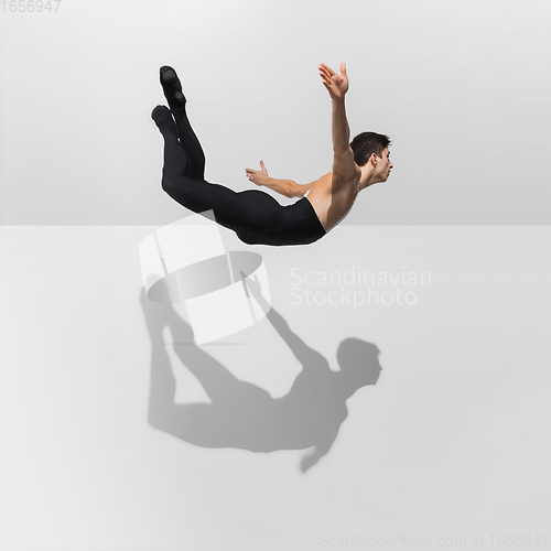 Image of Beautiful young male athlete practicing on white studio background with shadows in jump, air flying