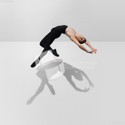 Image of Beautiful young male athlete practicing on white studio background with shadows in jump, air flying