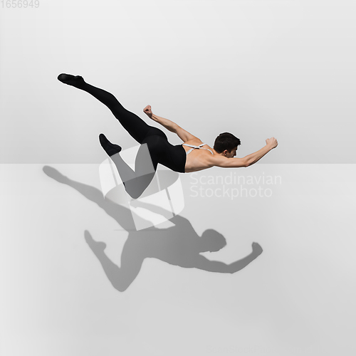 Image of Beautiful young male athlete practicing on white studio background with shadows in jump, air flying
