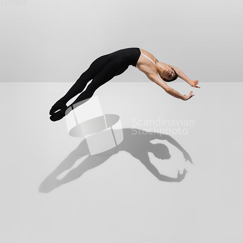 Image of Beautiful young male athlete practicing on white studio background with shadows in jump, air flying