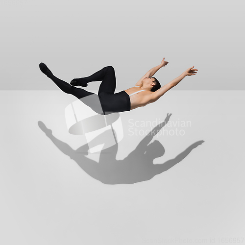 Image of Beautiful young male athlete practicing on white studio background with shadows in jump, air flying