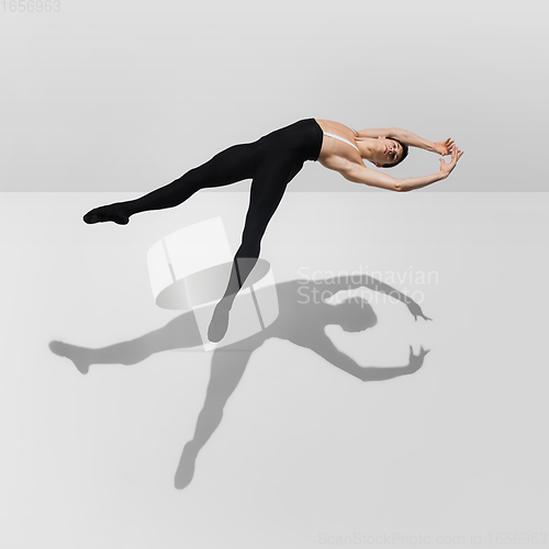 Image of Beautiful young male athlete practicing on white studio background with shadows in jump, air flying