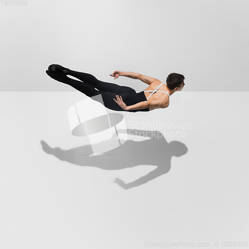 Image of Beautiful young male athlete practicing on white studio background with shadows in jump, air flying