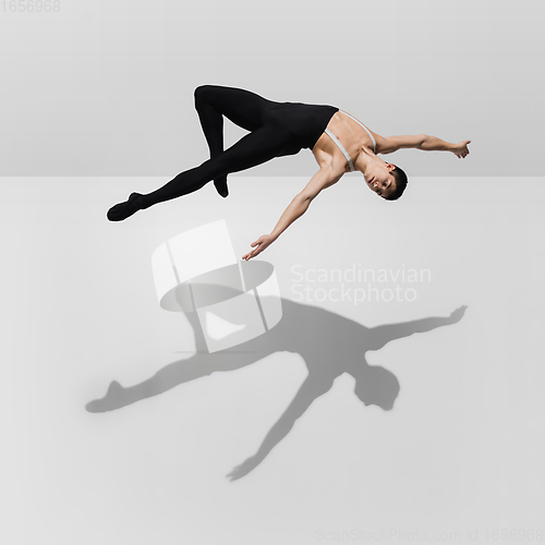 Image of Beautiful young male athlete practicing on white studio background with shadows in jump, air flying