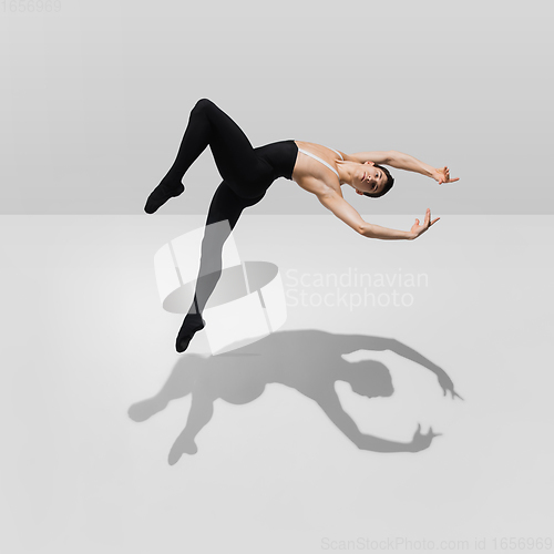 Image of Beautiful young male athlete practicing on white studio background with shadows in jump, air flying