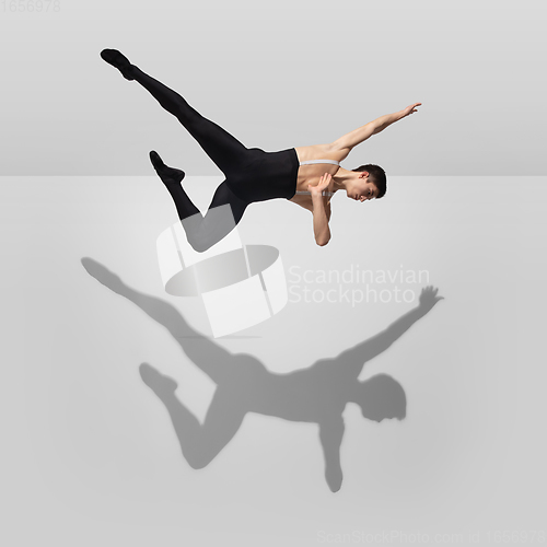 Image of Beautiful young male athlete practicing on white studio background with shadows in jump, air flying