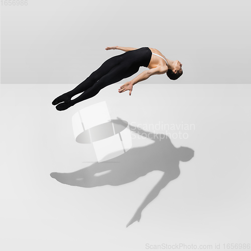 Image of Beautiful young male athlete practicing on white studio background with shadows in jump, air flying