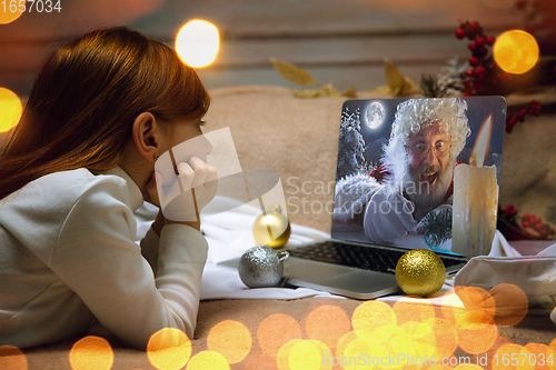 Image of Happy caucasian little girl during video call or messaging with Santa using laptop and home devices, celebration or ad flyer with copyspace