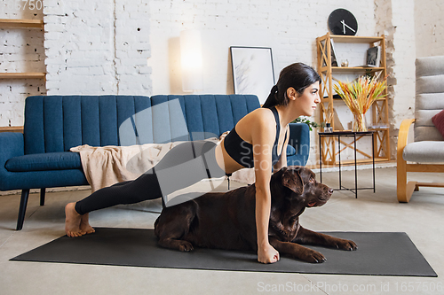 Image of Young woman working out at home during lockdown, yoga exercises with the dog