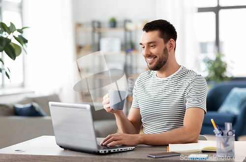 Image of man with laptop drinking coffee at home office