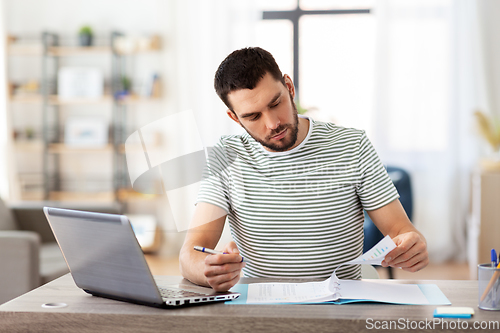 Image of man with papers and laptop working at home office