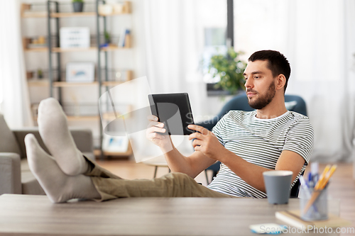 Image of man with tablet pc resting feet on table at home