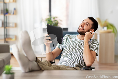 Image of happy man with tablet pc and earphones at home