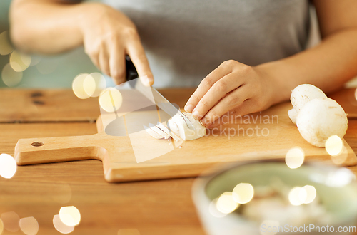 Image of woman cutting champignons by knife on board