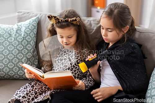 Image of girls in halloween costumes reading book at home
