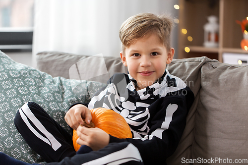 Image of boy in halloween costume with pumpkin at home