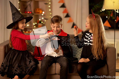 Image of kids in halloween costumes share candies at home