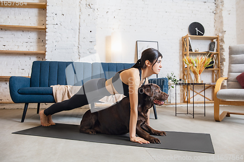 Image of Young woman working out at home during lockdown, yoga exercises with the dog