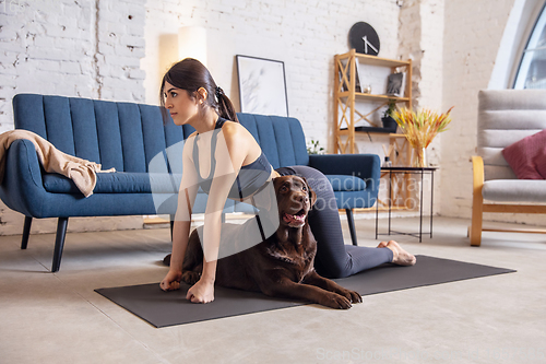 Image of Young woman working out at home during lockdown, yoga exercises with the dog