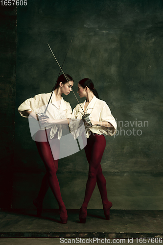 Image of Two young female ballet dancers like duelists with swords. Ballet and contemporary choreography concept. Creative art photo.