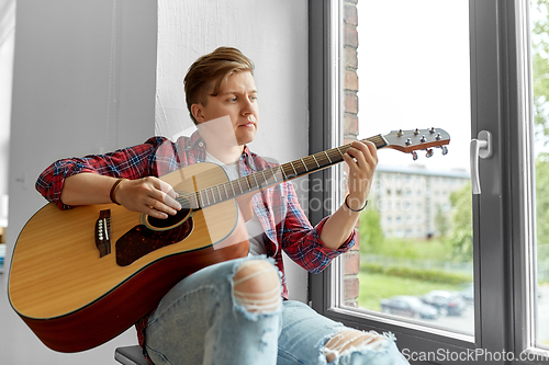 Image of young man playing guitar sitting on windowsill