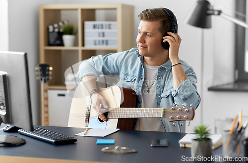 Image of man in headphones playing guitar at home