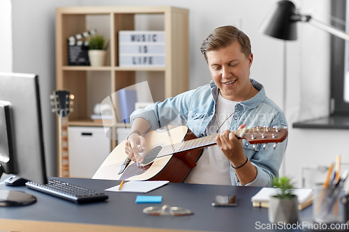 Image of young man playing guitar sitting at table at home