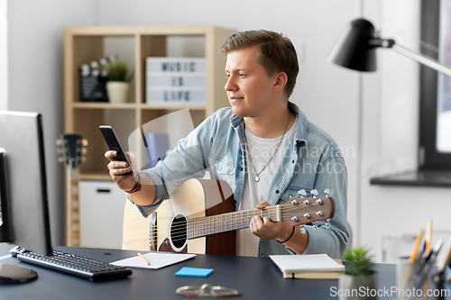 Image of young man with guitar and smartphone at home