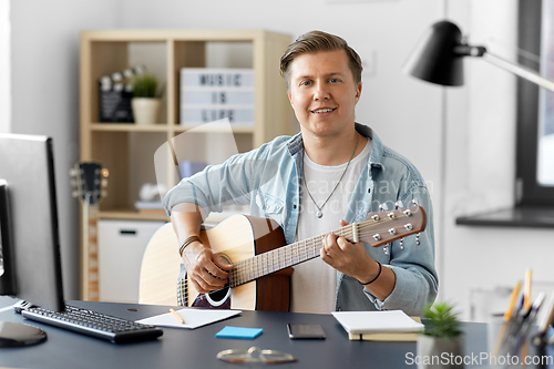 Image of young man playing guitar sitting at table at home