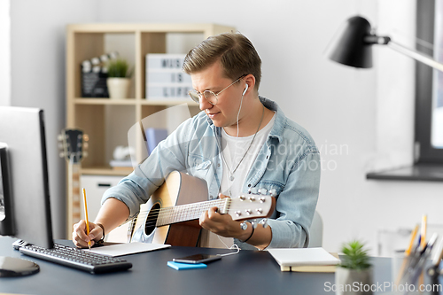 Image of man with guitar writing to music book at home