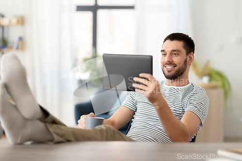 Image of man with tablet pc resting feet on table at home