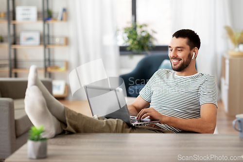 Image of happy man with laptop and earphones at home