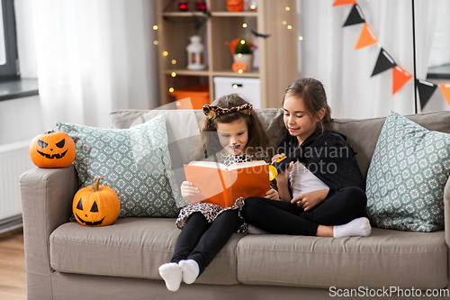 Image of girls in halloween costumes reading book at home