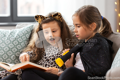 Image of girls in halloween costumes reading book at home