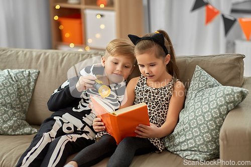 Image of kids in halloween costumes reading book at home