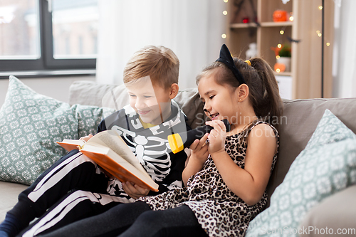 Image of kids in halloween costumes reading book at home