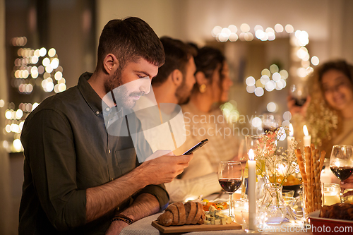 Image of man with smartphone at dinner party with friends