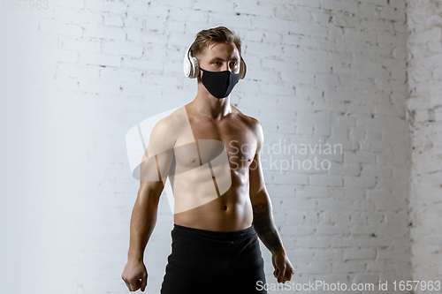 Image of Professional male athlete training on brick wall background wearing face mask. Sport during quarantine