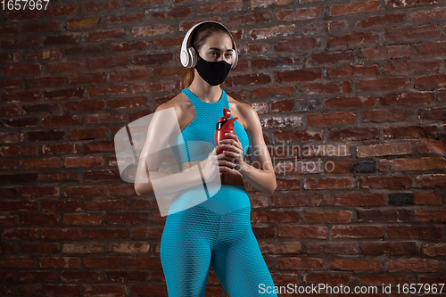 Image of Professional female athlete training on brick wall background wearing face mask. Sport during quarantine