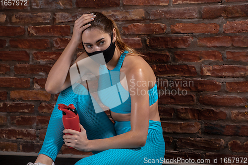 Image of Professional female athlete training on brick wall background wearing face mask. Sport during quarantine