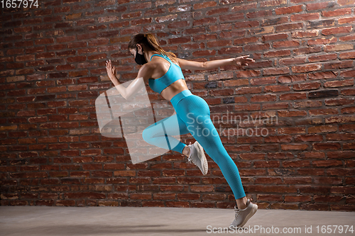 Image of Professional female athlete training on brick wall background wearing face mask. Sport during quarantine