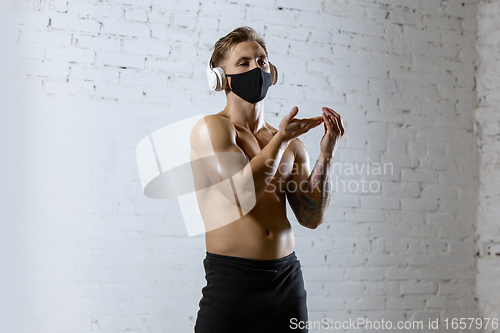 Image of Professional male athlete training on brick wall background wearing face mask. Sport during quarantine