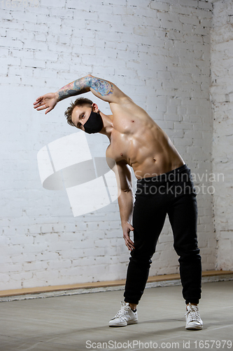 Image of Professional male athlete training on brick wall background wearing face mask. Sport during quarantine