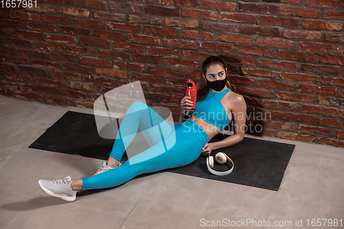 Image of Professional female athlete training on brick wall background wearing face mask. Sport during quarantine