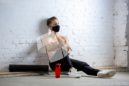 Image of Professional male athlete training on brick wall background wearing face mask. Sport during quarantine