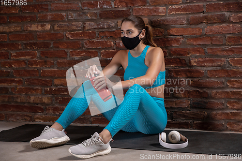 Image of Professional female athlete training on brick wall background wearing face mask. Sport during quarantine