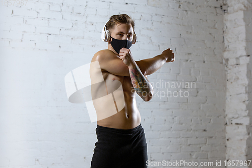 Image of Professional male athlete training on brick wall background wearing face mask. Sport during quarantine